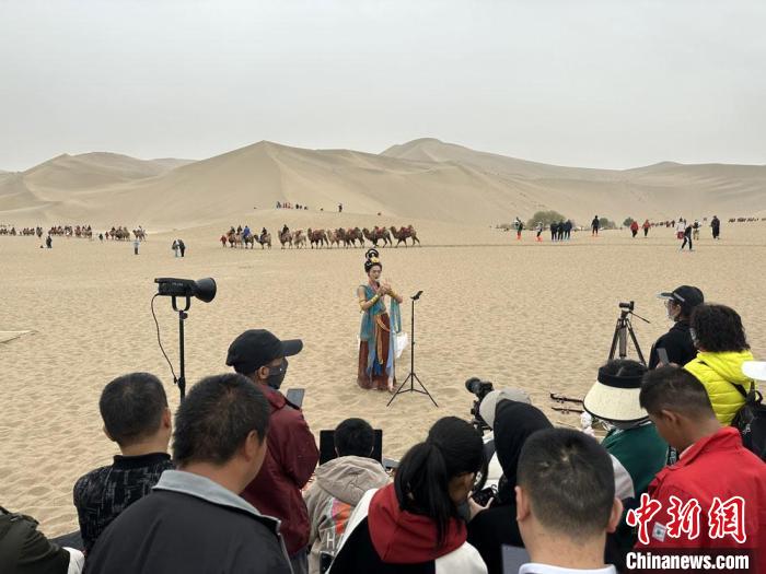 圖為2023年4月底，敦煌大漠“逐舞者”奧楠在鳴沙山月牙泉景區(qū)視頻直播，吸引游人圍觀?！●T志軍 攝