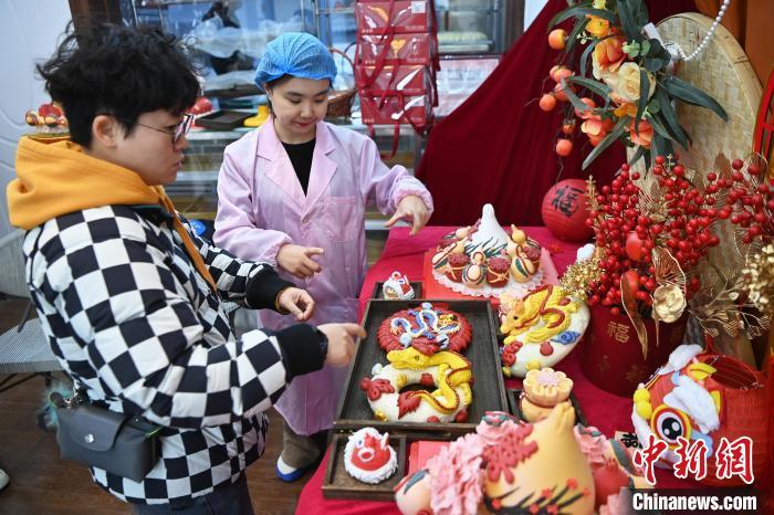 1月25日，隨著春節(jié)臨近，蘭州一花饃店“龍”元素花饃熱銷。圖為工作人員向顧客推薦“龍”元素花饃。九美旦增 攝</p><p>